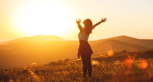 Happy woman jumping and enjoying life in field at sunset in mountains